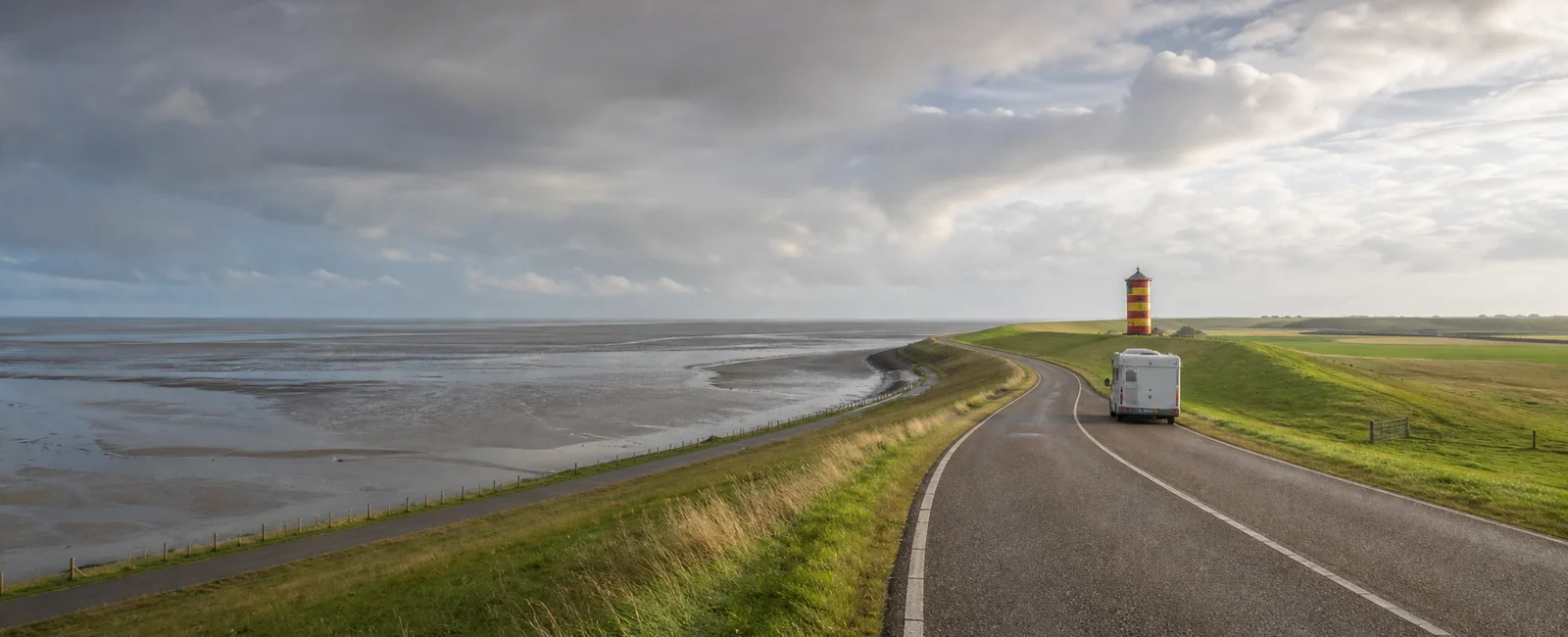 KI-generiertes Routenmotiv: Reisemobil an der Nordseeküste mit Deich, Wattenmeer und Leuchtturm