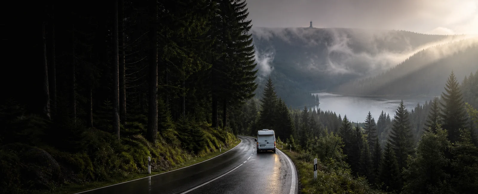 KI-generiertes Routenmotiv: Reisemobil auf nasser Schwarzwaldstraße zwischen Tannen, Nebel und Bergsee